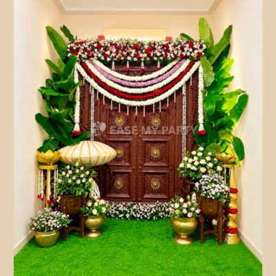 Traditional wooden door naming ceremony decoration with fresh jasmine garlands, banana leaves, brass urlis, and name reveal shell prop in Bangalore by EaseMyParty