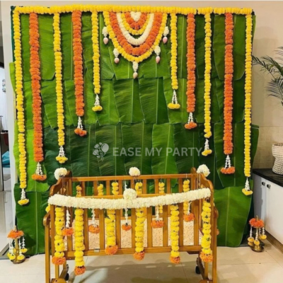 Traditional banana leaf backdrop with fresh yellow orange marigold drops, lotus bud toran, and rental cradle for naming ceremony in Bangalore by Ease My Party