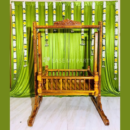 Traditional hand carved wooden cradle rental with green satin curtain backdrop and yellow white flower garlands for naming ceremony in Bangalore by Ease My Party