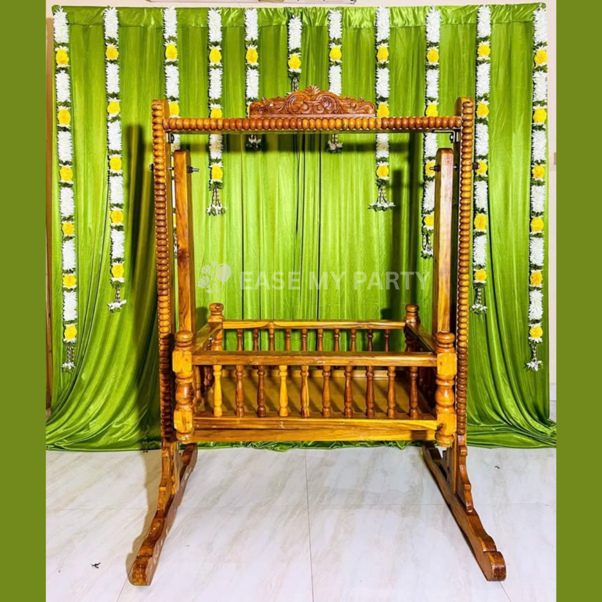 Traditional hand carved wooden cradle rental with green satin curtain backdrop and yellow white flower garlands for naming ceremony in Bangalore by Ease My Party