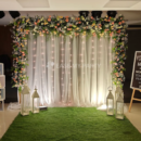 Alt Text: White galaxy netted backdrop with natural peach rose and gypsophila flower arch, fairy lights, lanterns, and green carpet matting for naming ceremony in Bangalore by Ease My Party